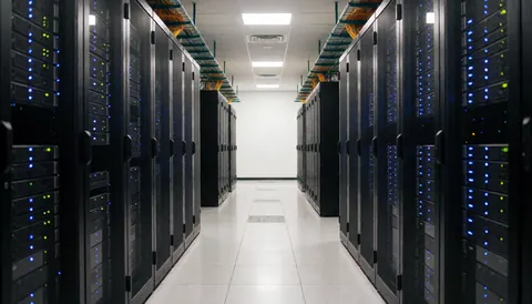 Allée entre des rangées de serveurs avec éclairage bleu, plafond avec câblage visible et sol poli reflétant la lumière.