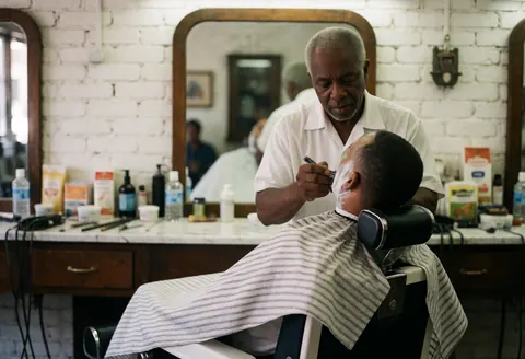 Un barbier expérimenté effectue une coupe de cheveux et un rasage professionnel sur un client assis dans un fauteuil de barbier.