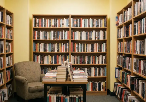 Vue intérieure d'une librairie accueillante présentant des étagères chargées de livres, une table et une chaise invitant à la lecture dans un cadre confortable.