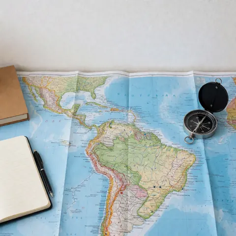 Une carte de l'Amérique du Sud posée sur une surface, accompagnée d'une boussole, d'un carnet et d'un stylo pour la planification de voyages.