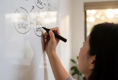Une femme professionnelle écrit une carte mentale sur un tableau blanc dans un bureau moderne éclairé par la lumière naturelle.
