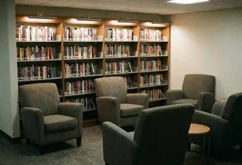Coin lecture confortable doté de fauteuils moelleux et d'étagères remplies de livres, baigné d'une lumière chaleureuse pour un travail serein en coworking.