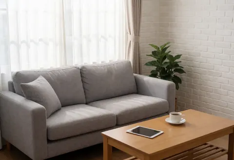 Un salon lumineux avec un canapé gris, une table en bois portant une tablette et du café, mur de briques blanches, rideaux et plante, ambiance relaxante pour travailler à domicile.