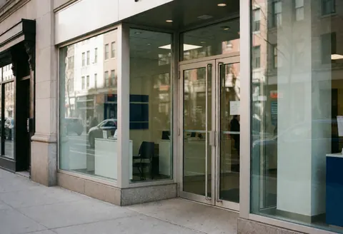 Façade contemporaine d'un bureau de comptabilité avec portes en verre reflétant la rue, révélant un intérieur professionnel et épuré.