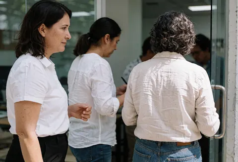 Trois femmes dans un bureau moderne, une guide l'autre près d'une porte vitrée avec lumière naturelle.