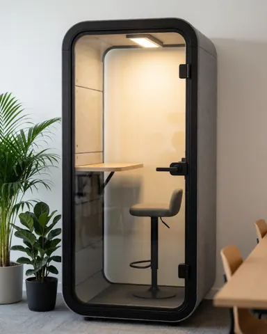 Cabine insonorisée équipée d'un bureau et d'une chaise, éclairage chaleureux, plante verte, design moderne pour travailler en privé.
