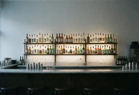 Vue de l'intérieur d'un bar moderne et minimaliste, avec une barre en bois, des bouteilles et des verres disposés sur le comptoir, prêt à accueillir les clients.