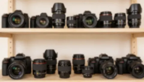 Arrière-plan flou d'une étagère de studio contenant plusieurs objectifs et appareils photo, aux tons chauds, idéal pour ajouter du texte ou pour le design graphique.