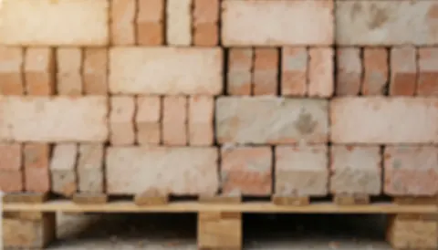 Arrière-plan texturé montrant des briques empilées sur une palette en bois, évoquant un chantier de construction avec du ciment et des matériaux de bâtiment.