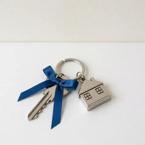 Porte-clés blanc en forme de maison posé sur un fond blanc uni, symbolisant l'immobilier et la propriété.