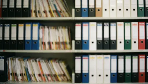 Des étagères avec des classeurs colorés sur un fond doux et professionnel pour du texte dans un bureau comptable calme et ordonné.