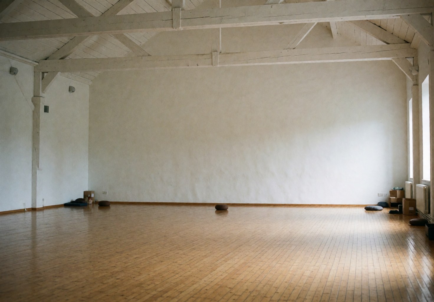 Salle de yoga vide dotée d'un sol en bois poli, de poutres en bois exposées et de murs blancs, offrant un cadre idéal pour la pratique et la méditation dans une ambiance calme et naturelle.