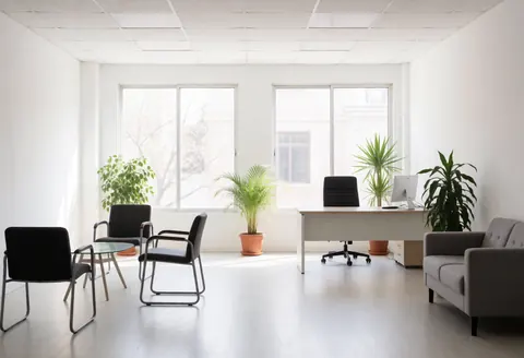 Espace de travail vide avec mobilier contemporain, plantes vertes, grandes fenêtres et murs blancs baignés de lumière naturelle pour un cadre professionnel.