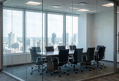 Vue d'une salle de réunion moderne et vide, équipée d'une table de conférence et de chaises, baignée de lumière naturelle par de grandes fenêtres offrant une perspective urbaine.