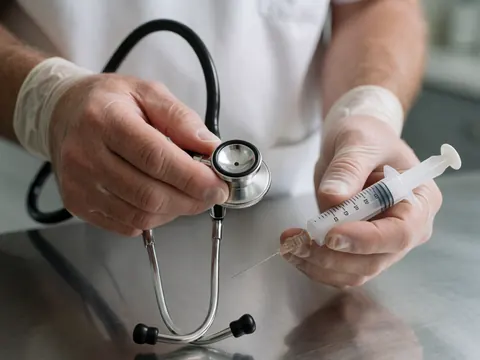 Mains portant des gants blancs tenant un stéthoscope et une seringue sur une table d'examen métallique dans un contexte clinique vétérinaire professionnel.