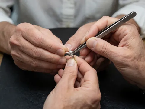 Gros plan montrant un diamant en cours de montage sur une monture en argent, avec des pinces et des outils de joaillerie sur un fond sombre.
