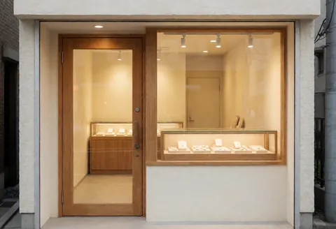 Façade d'une boutique de bijoux avec vitrine et porte en bois, murs crème, éclairage chaleureux créant une ambiance professionnelle et accueillante.