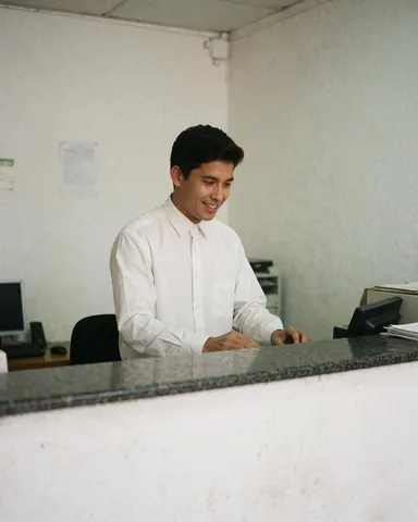 Employé de banque souriant derrière un comptoir, attentif à son travail, dans un environnement professionnel et accueillant avec des murs blancs.