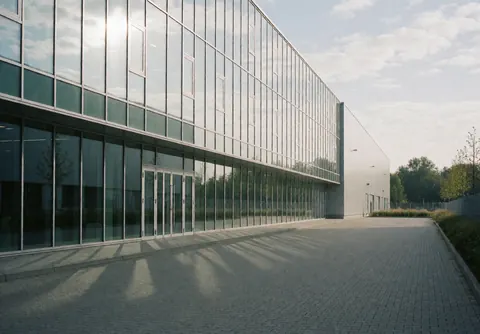 Vue extérieure d'une façade de bâtiment industriel avec des fenêtres en verre reflétant le ciel et les nuages.