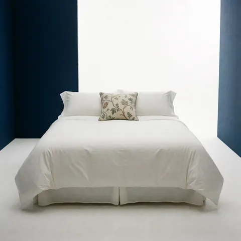 Lit king size ou matrimonial avec draps blancs impeccables, coussin décoratif, fond bleu clair et ambiance minimaliste de luxe hôtelier.