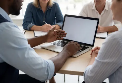 Une personne présente un document lors d'une réunion en bureau moderne avec lumière naturelle sur table en bois.