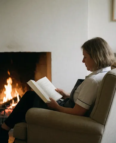 Une cliente profite de la tranquillité en lisant un livre confortablement installée dans un fauteuil à côté d'une cheminée allumée.