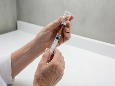 Des mains d'adulte préparent une injection en remplissant une seringue à partir d'un flacon médical sur un fond clinique propre et neutre.