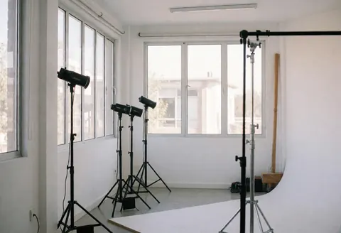 Studio photographique aux murs blancs, grandes fenêtres apportant une lumière naturelle, éclairage professionnel et fond blanc pour services photo.