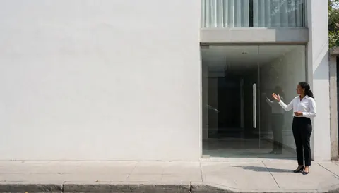 Une agente immobilière professionnelle se tient debout devant l'entrée vitrée d'un bâtiment contemporain en journée.