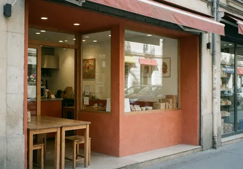 Façade d'un restaurant aux murs en terre cuite, grandes fenêtres et tables en bois. L'intérieur est visible, l'ambiance est chaleureuse et propre.