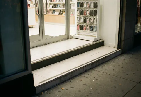 Façade moderne d'un commerce avec une porte vitrée et un petit marchepied pour faciliter l'accès, éclairage intérieur visible à travers la vitrine.