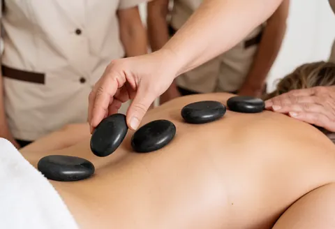 Un thérapeute utilise des pierres de basalte chauffées pour réaliser un massage relaxant sur le dos nu d'un client dans un cadre spa apaisant.
