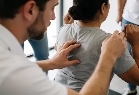 Un entraîneur personal trainer ajuste la position du dos d'un client lors d'une séance de coaching en gymnase pour améliorer sa posture.