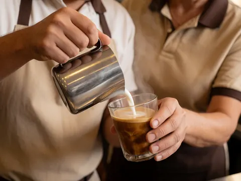 Mains d'un barista versant du lait chaud dans une tasse de café avec de la vapeur visible en gros plan.