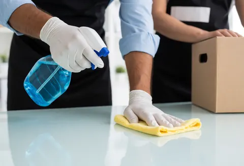 Une personne effectue le nettoyage d'un bureau en utilisant un pulvérisateur et un chiffon en microfibre pour assurer la désinfection.