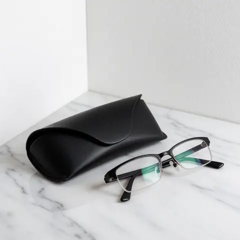 Paire de lunettes de lecture à monture noire posée avec son étui noir sur une surface en marbre blanc, éclairage doux et composition minimaliste.
