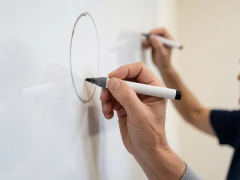 Une main adulte trace un cercle avec un marqueur sur un tableau blanc propre et moderne, évoquant la planification professionnelle.