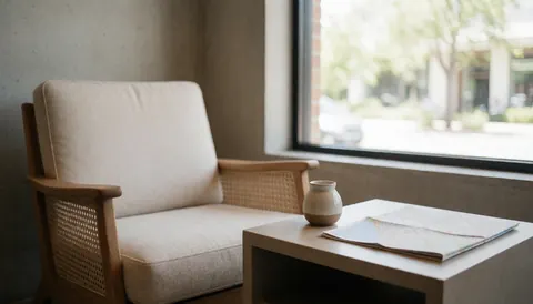 Vue du hall spacieux et accueillant d'un hôtel, éclairé par la lumière naturelle, avec un fauteuil confortable, une table basse supportant une carte et des objets en céramique.