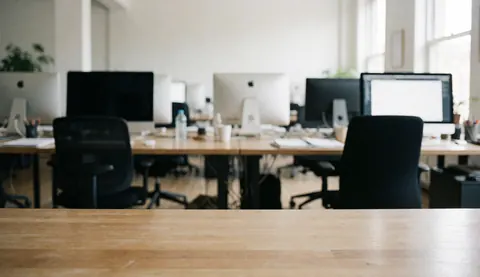Un espace de travail moderne et lumineux avec un bureau, une chaise et un ordinateur placé près d'une grande fenêtre laissant entrer la lumière du jour.