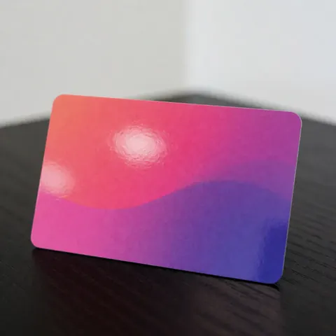 Une carte aux couleurs vives dégradées rose et violet posée sur une surface en bois clair avec un reflet subtil sur un fond blanc.