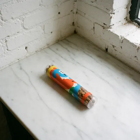 Tube coloré pour friandises canines posé sur un comptoir en marbre blanc avec un mur de briques blanches en arrière-plan et une lumière naturelle.
