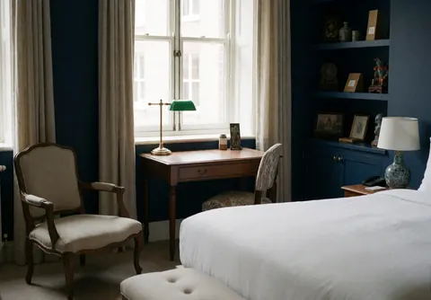 Suite d'hôtel spacieuse équipée d'un lit confortable, d'une chaise et d'un bureau, aux murs bleus, baignée de lumière naturelle avec une décoration culturelle.