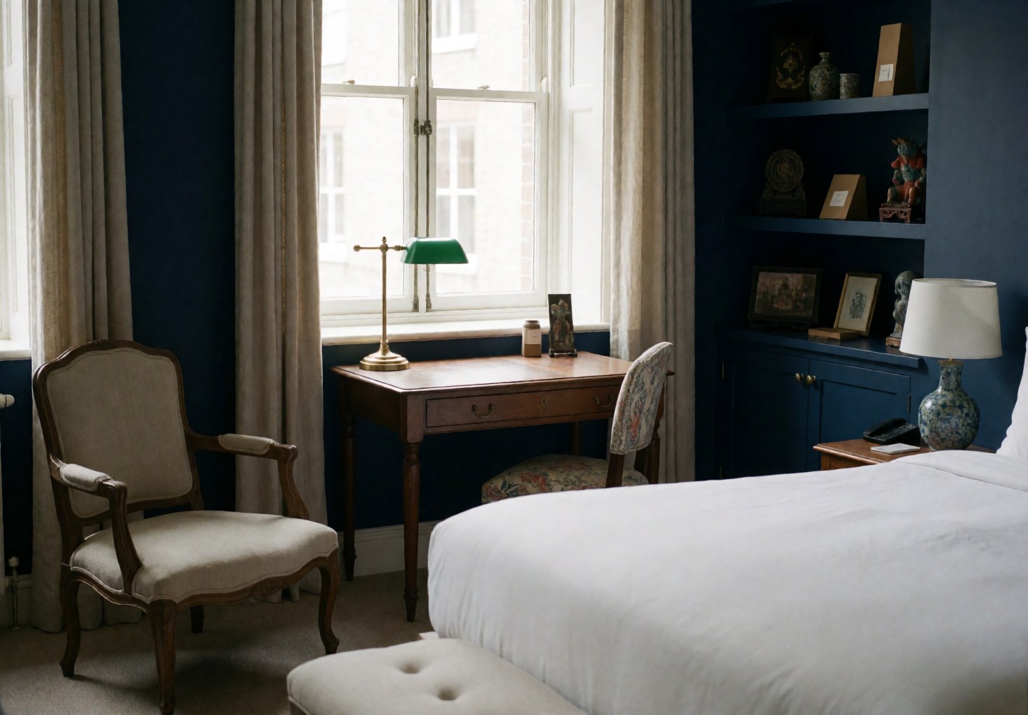 Suite d'hôtel spacieuse équipée d'un lit confortable, d'une chaise et d'un bureau, aux murs bleus, baignée de lumière naturelle avec une décoration culturelle.