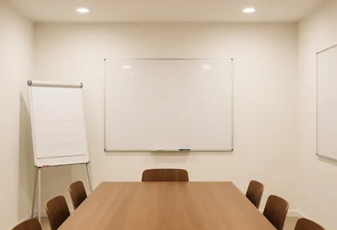 Salle de réunion moderne équipée d'une table en bois, de chaises et de tableaux blancs, idéale pour les affaires et la planification stratégique dans un environnement professionnel.