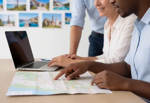 Un agent de voyages et un client consultent ensemble une carte sur un ordinateur dans un bureau lumineux pour planifier un déplacement professionnel.