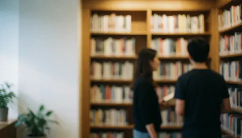 Des étagères en bois chargées de livres baignées d'une lumière chaude, avec des murs blancs et quelques plantes vertes, créant une ambiance calme propice à la lecture.