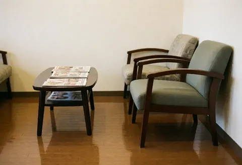 Vue latérale de l'intérieur d'un salon de barbier avec des chaises, une table, des magazines et un sol en bois poli.