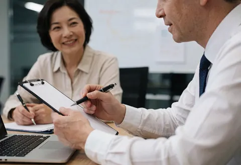 Un stratège expose des résultats à un client dans un bureau bien éclairé, tous deux avec des ordinateurs et des carnets.