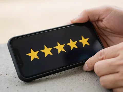 Une main tenant un smartphone affichant cinq étoiles jaunes sur un écran, posé sur une surface en béton, évoquant la satisfaction client et le marketing digital.