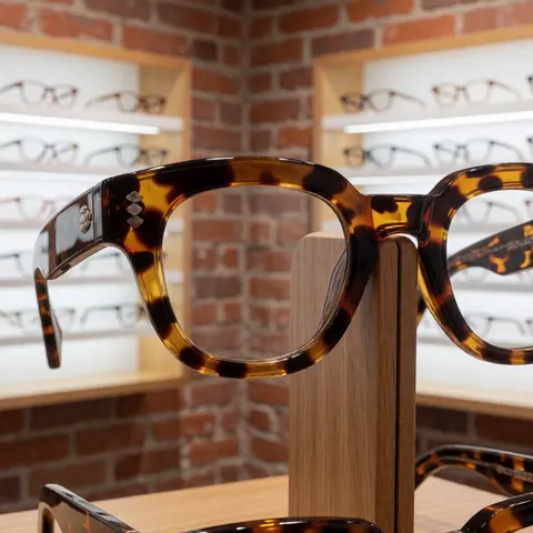 Présentation de montures en acétate pour lunettes sur un comptoir d'optique avec éclairage professionnel mettant en valeur le design et la qualité du produit.